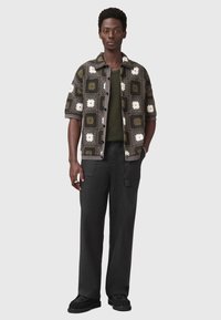 Camicetta a maniche corte con bottoni in verde scuro e grigio, decorata con un motivo in pizzo floreale bianco, abbinata a pantaloni scuri e scarpe nere con texture.