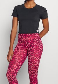 Zwart cropped sporttopje met korte mouwen en een roze logo; roze legging met luipaardprint, hoge taille en een gestructureerd patroon.