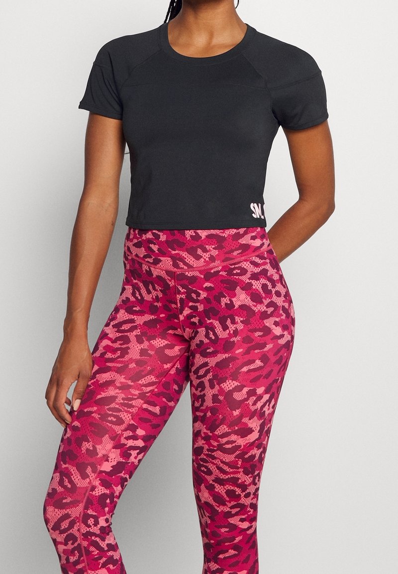 Zwart cropped sporttopje met korte mouwen en een roze logo; roze legging met luipaardprint, hoge taille en een gestructureerd patroon.