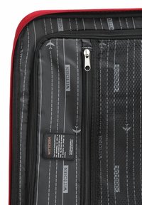 Interno di una valigia morbida rossa con tessuto nero decorato con aerei bianchi e segnaletica stradale, scomparti con zip e un'etichetta del marchio.