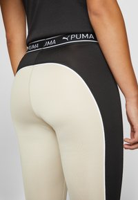 Leggings visokog struka s crnim pojasom s "PUMA" logotipom. Dizajn boja u crnoj i krem nijansi, s bijelim detaljima i glatkom teksturom.