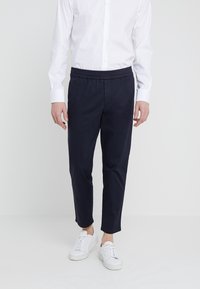 Niebieskie spodnie z bawełny z elastycznym paskiem, zwężane nogawki i kieszeniami, w zestawieniu z białymi sneakersami oraz białą koszulą zapinaną na guziki.