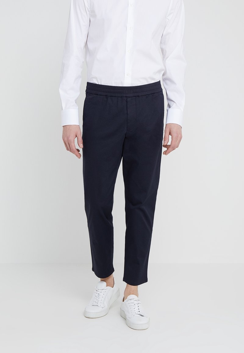 Niebieskie spodnie z bawełny z elastycznym paskiem, zwężane nogawki i kieszeniami, w zestawieniu z białymi sneakersami oraz białą koszulą zapinaną na guziki.