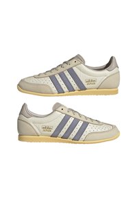 Szare i kremowe skórzane sneakersy z trzema niebieskimi paskami, perforowanym wzorem i beżową gumową podeszwą. Logo widoczne z boku.