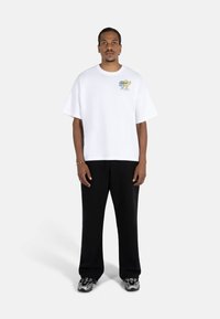 White oversized t-shirt with short sleeves, featuring colorful cartoon-style embroidery near the chest, paired with black wide-leg pants.