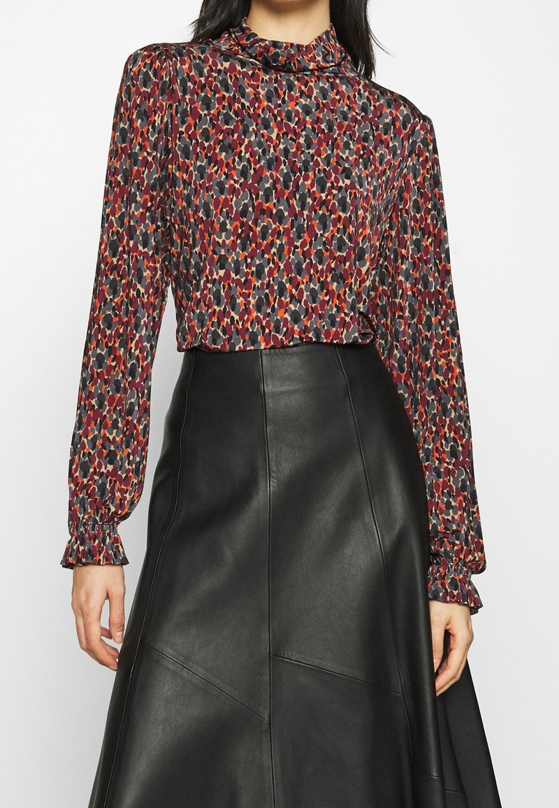 Langarmoberteil mit hohem Kragen, das ein mehrfarbiges abstraktes Muster auf einem dunklen Stoff zeigt, kombiniert mit einem schwarzen, ledernen A-Linien-Rock.
