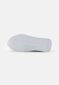 Suela de zapatilla blanca con un patrón de llanta en zigzag. Presenta una superficie texturizada y una etiqueta de la marca ligeramente elevada en el centro.
