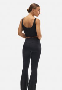 Top deportivo negro con espalda de corte amplio y tirantes gruesos, combinado con leggings negros de campana. Textura suave y diseño ajustado.
