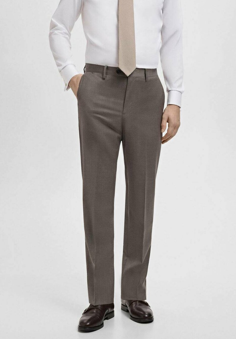Pantalon gris en tissu lisse, présentant une coupe droite et des poches latérales, associé à des chaussures foncées et une cravate claire.