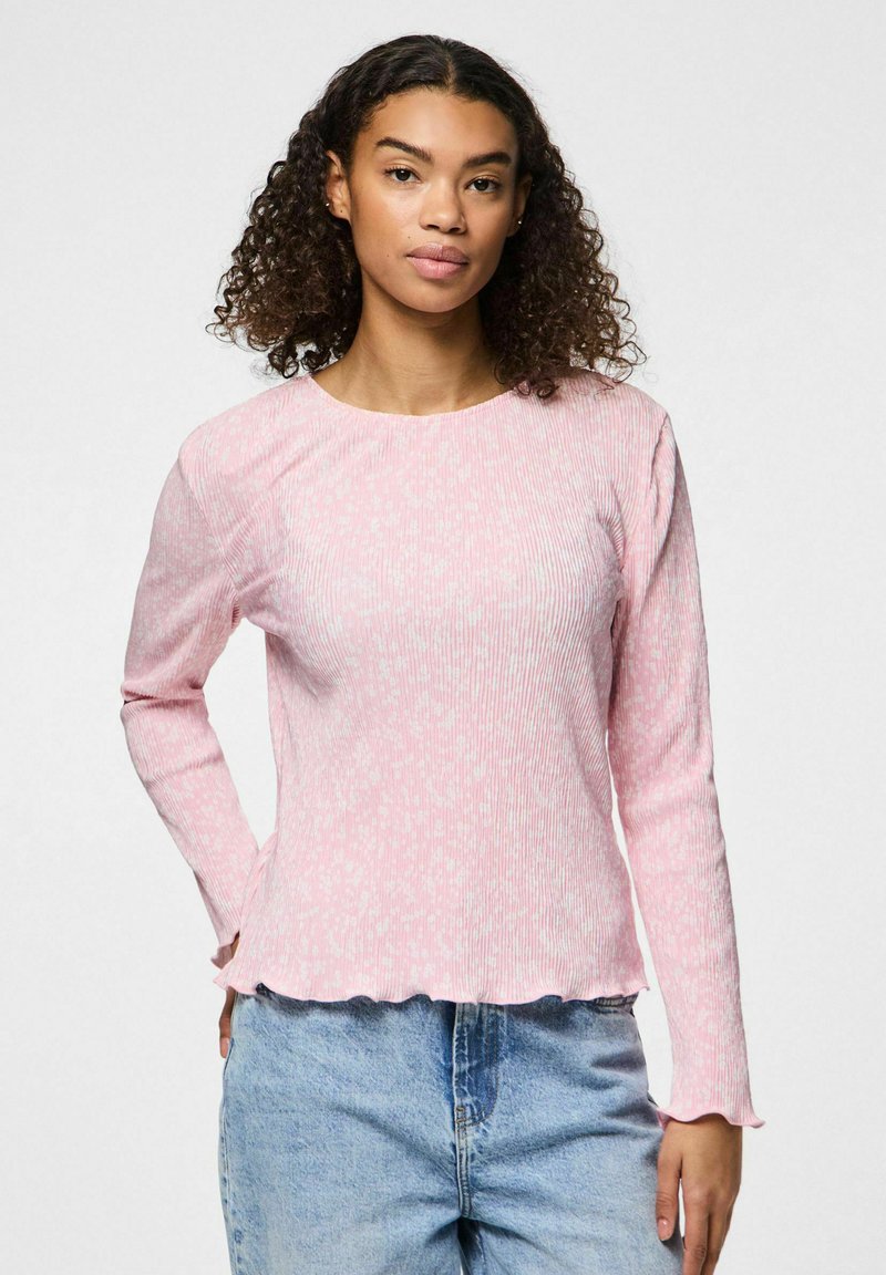 Garās piedurknes rozā ribota krekls ar teksturētu apdari, ar apaļu apkakli un viļņotu apakšmalu, apvienots ar gaiši ziliem džinsiem.