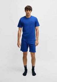 Blue crew-neck t-shirt with short sleeves, plain texture; paired with matching shorts. Black logo detail visible on the shirt.