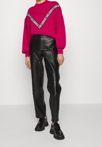 Fuksjowa bluza z czarnym logo, zestawiona z wysokim stanem czarnymi skórzanymi spodniami z zamkami i sięgającymi kostek masywnymi czarnymi butami.
