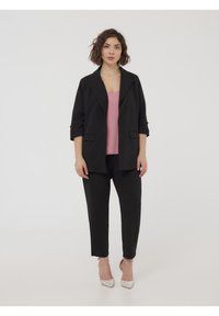 Blazer nero con maniche arrotolate, abbinato a un top rosa e pantaloni neri. Accentuato con tacchi argentati, caratterizzati da un design elegante e moderno.