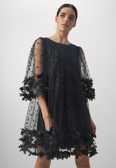 Rochie neagră dintr-un material transparent, cu motive stelare și aplicații florale la mână și tiv, având o siluetă fluidă și lejeră.