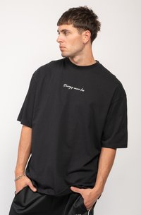 Black cotton t-shirt with short sleeves, round neckline, and embroidered text “Energy never lies” in white on the front.
