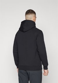 Sudadera negra con capucha grande y suave, mangas raglán y dobladillo acanalado. La tela parece suave, con un color sólido y mínimas adornos.