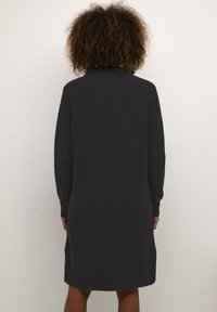 Robe en tricot noire avec un col haut, des manches longues et une coupe décontractée, présentant un tissu texturé et des poignets et ourlet en côtes.