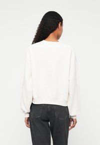 Lys kremfarget genser med crew neckline, oversized ermer og ribbet kant. Brukt over mørkegrå høywaistet jeans.