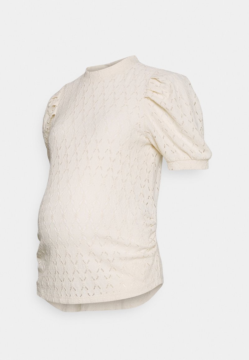 Jasnokremowy top ciążowy z fakturą w diamentowy wzór, krótkimi bufkami, okrągłym dekoltem i marszczonymi detalami po bokach.
