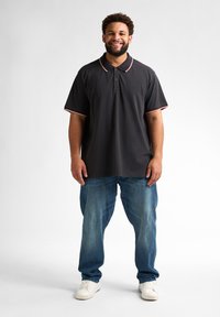 Czarna koszulka polo z czerwonym i białym wykończeniem przy kołnierzyku i rękawach, w zestawieniu z jasnoniebieskimi dżinsami i białymi trampkami. Luźny fason i styl.