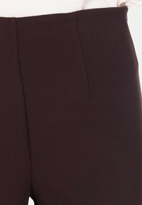 Pantaloni tagliati marrone scuro realizzati in tessuto liscio, con una parte frontale pulita, una piega sottile e senza hardware o accenti visibili.