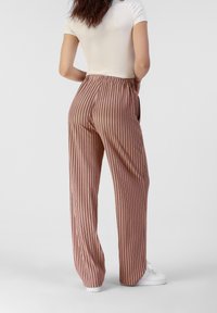 Pruhované, vysoké kalhoty z měkké růžové látky s volným střihem. Obsahují elastický pas a vertikální pruhy pro vzdušný vzhled.