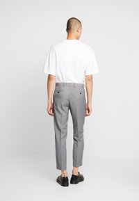 Grijze op maat gemaakte broek van gestructureerde stof, met een slim fit, riemlussen en twee achterzakken. Draagt een effen wit t-shirt.