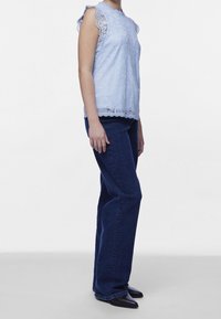 Ljusblå spetsblus med vågiga kanter, parat med mörkblå utsvängda jeans och svarta korkade skor.