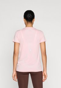 Lys rosa trenings t-skjorte med rund hals, korte ermer og teksturerte detaljer på ryggen. Materialet ser ut til å være pustende og elastisk.
