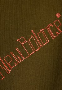 Olivgrüner Stoff mit auffälligem, pink gesticktem "New Balance"-Logo. Die Textur ist glatt und hat ein eng gestricktes Muster.