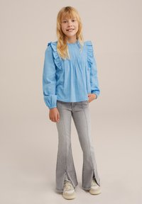 Svijetloplava bluzica s dugim rukavima i nabranim detaljima, uparena s svijetlosivim trapericama s otvorima sa strane i bež patikama.