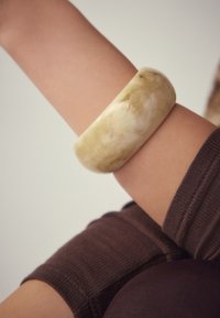 Translucent greenish-white resin bangle on a light skin tone arm, paired with a dark brown ribbed sleeve. Smooth, polished surface.