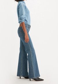 Jean en denim bleu clair avec une coupe évasée, taille haute et surpiqûres contrastantes, associé à une veste en denim assortie.