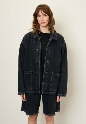 Zwarte denim oversized jas met voorzakken en knoopsluiting, gecombineerd met bijpassende zwarte denim shorts met rafelrand.