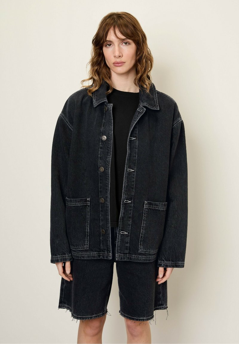 Zwarte denim oversized jas met voorzakken en knoopsluiting, gecombineerd met bijpassende zwarte denim shorts met rafelrand.