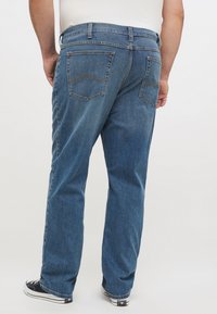 Blå denimjeans med en avslappnad passform, som har två bakfickor, synlig sömnad och rak bendesign. Bärs med svarta sneakers.