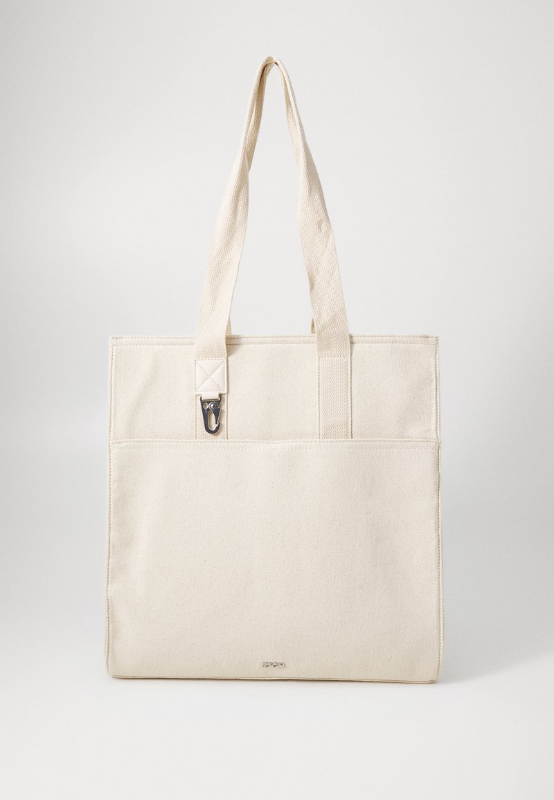 Canvas tote bag in soft beige with two sturdy handles, a front pocket, and metal hardware detail. Smooth texture and rectangular shape.