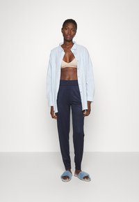 Lichtblauw en wit gestreepte button-up shirt, beige bralette, marineblauwe broek en blauwe gezellige slippers, gestyled in een relaxte pasvorm.