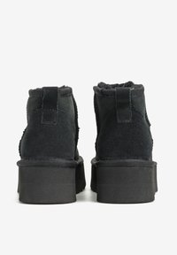 Czarne botki zamszowe z teksturowanym wykończeniem, zaokrąglonym noskiem i grubą czarną gumową podeszwą. Wyposażone w pętlę na pięcie ułatwiającą zakładanie.