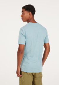 Camiseta de algodón azul claro con cuello redondo y mangas cortas, que presenta una textura suave y un diseño simple, sin adornos.
