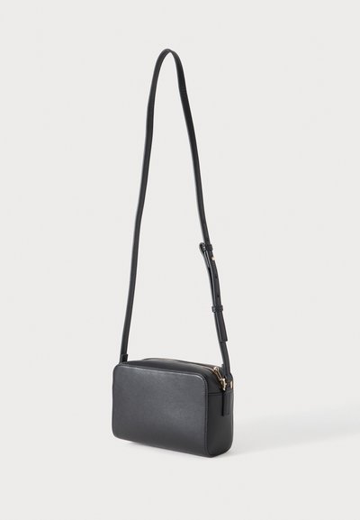Sac bandoulière rectangulaire noir avec bandoulière longue réglable et fermeture éclair dorée sur fond clair uni.