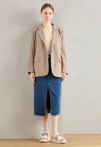 Beige blazer, fitted design with pockets, paired with a knee-length blue denim skirt featuring a front slit. Light sandals with thick soles.