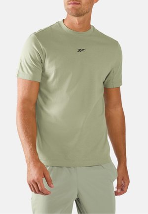 Mann trägt hellgrünes kurzärmeliges T-Shirt mit kleinem schwarzem Logo auf der Brust und passende hellgrüne Shorts vor weißem Hintergrund.