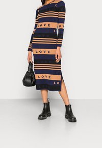 Robe en tricot avec des rayures bleu marine et beige, portant le mot « LOVE » à divers emplacements, à manches longues et avec une fente sur le côté.