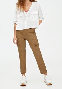 Chemise blanche à boutons, coupée, avec deux poches poitrine, associée à un pantalon cargo marron avec des détails de poche et une coupe ajustée. Baskets blanches.