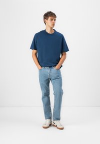Navyblauwe katoenen t-shirt met een ronde hals, korte mouwen, gecombineerd met lichtblauwe denim jeans en witte sneakers met bruine zolen.