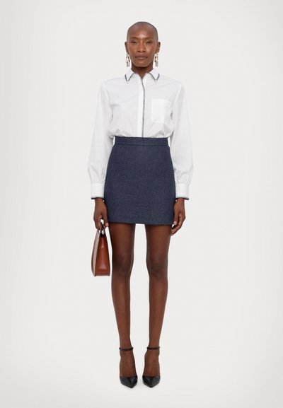 White shirt with a pocket and contrasting trim, paired with a dark denim skirt. Accessories include hoop earrings and a brown handbag.