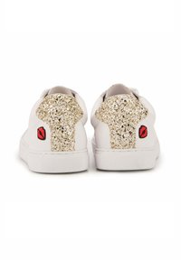 Baskets blanches avec des accents dorés scintillants sur le talon. Présentent des graphiques de lèvres rouges de chaque côté. Matériau lisse et forme classique.