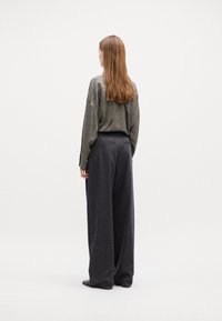 Graues Karomuster Oversize-Hemd mit langen Ärmeln, kombiniert mit weiten, dunkelgrauen Hosen. Weiche Texturen und ein elegantes Design.