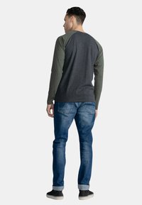 Langærmet skjorte med en mørkegrå krop og olivengrønne raglanærmer, parret med blå denimjeans og sorte slip-on sko.